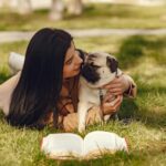 女子躺在草地上親密擁抱哈巴狗，旁邊放著一本攤開的書籍